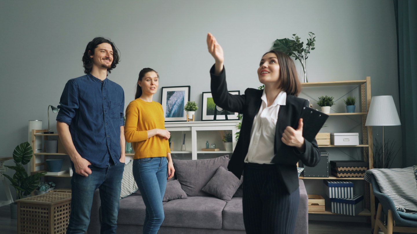 Real estate agent shows modern living room to couple.